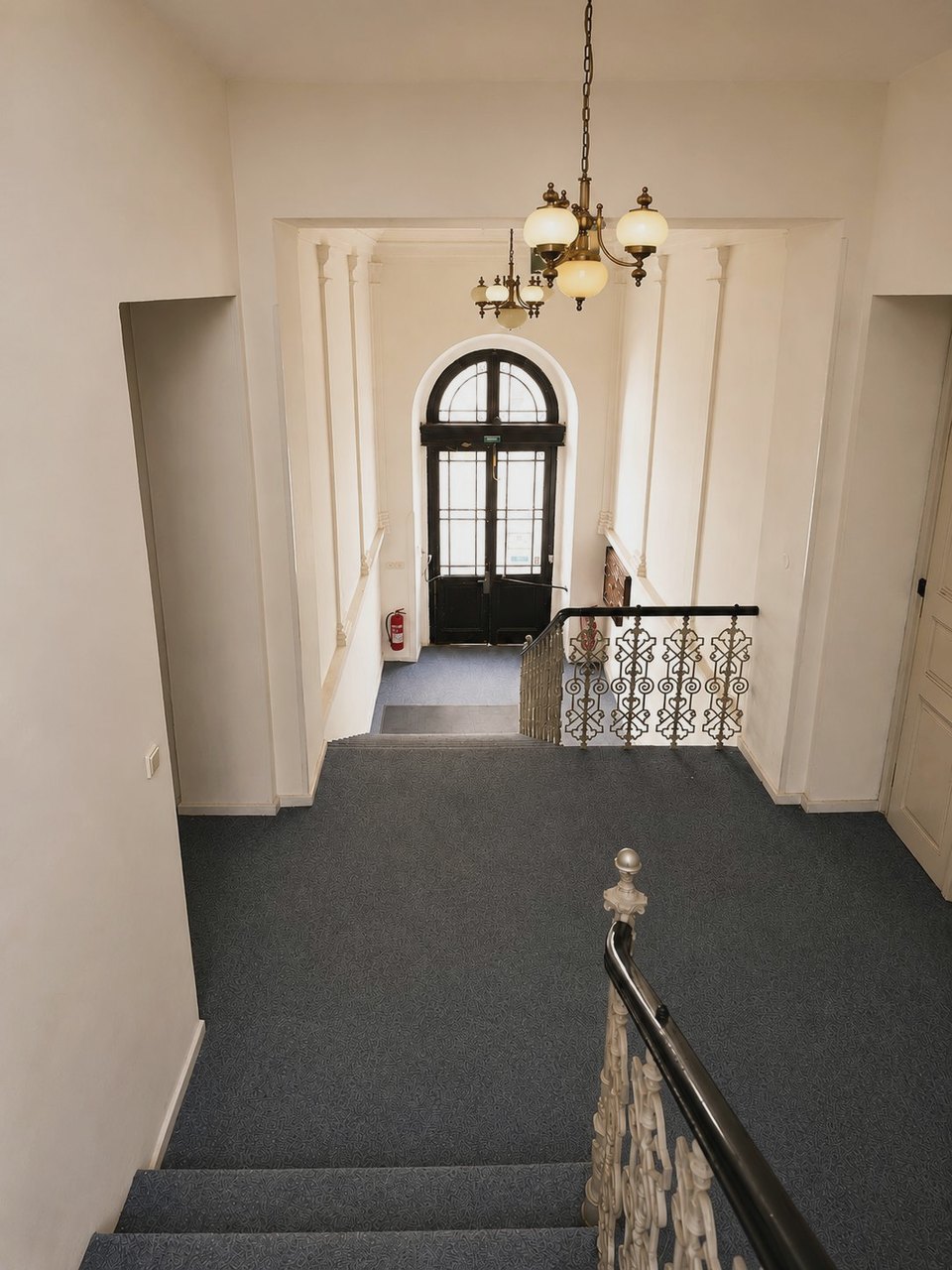 Historic staircase with a wrought-iron railing and a chandelier