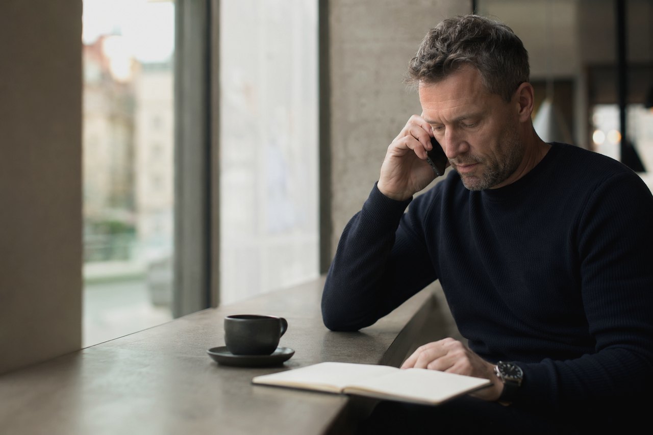 Entrepreneur on the phone taking notes in a notebook by a window overlooking Prague rooftops