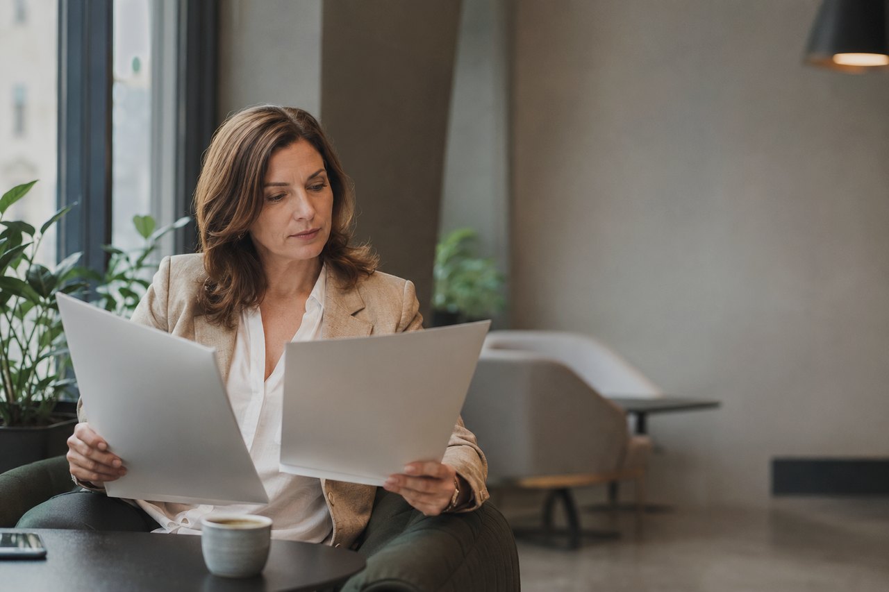 Businesswoman in a light blazer reading documents in a calm office by the window, a cup of coffee on the table